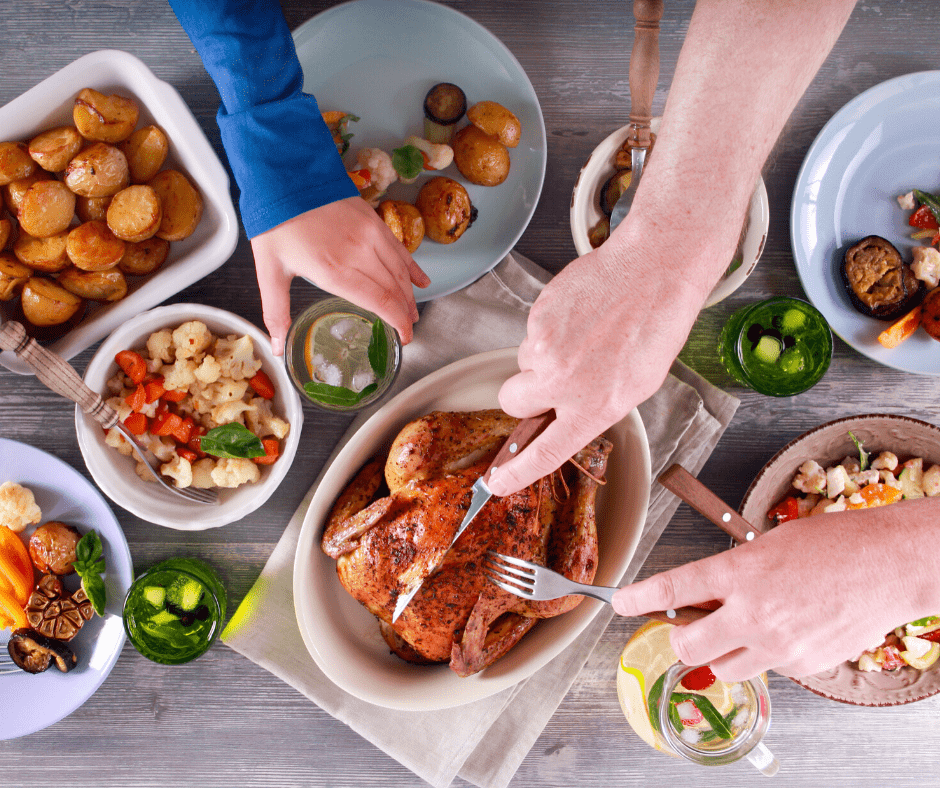 Hands carve a turkey on a dinner table with plates, drinks and side dishes